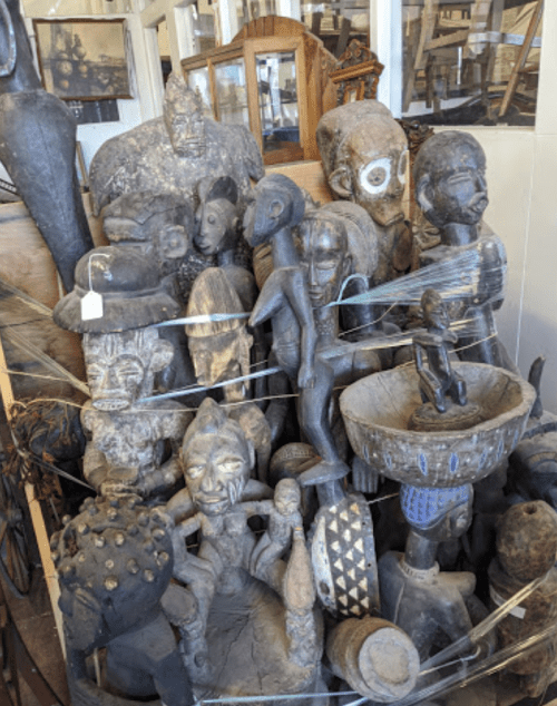 A collection of various carved wooden sculptures and artifacts displayed in a cluttered antique shop.
