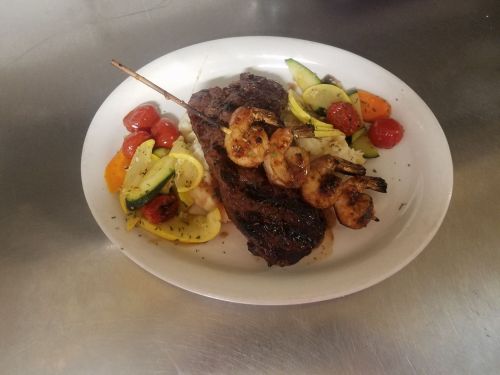 A plate featuring grilled steak, shrimp skewers, and a colorful medley of sautéed vegetables.