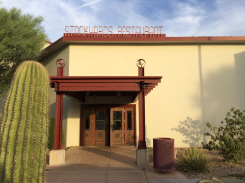 Entrance of Stockyards Restaurant with a cactus and landscaping in front, under a clear blue sky.