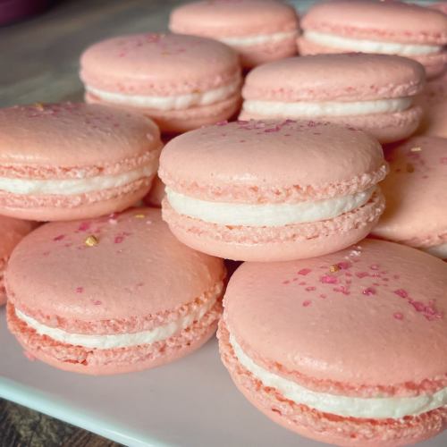 A close-up of pink macarons with white filling, sprinkled with pink sugar, arranged on a white plate.