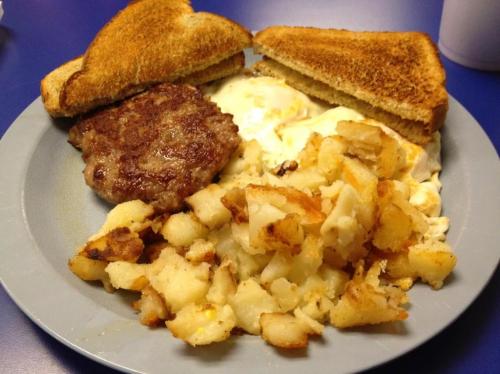 A plate of breakfast featuring toast, scrambled eggs, sausage patty, and crispy hash browns.