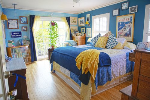 Brightly decorated bedroom with blue walls, a cozy bed, and large windows letting in natural light.