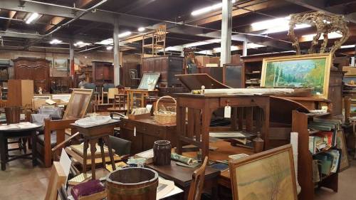 A cluttered antique store filled with various wooden furniture, paintings, and decor items.