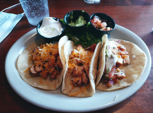 Three tacos filled with chicken, cheese, and toppings, served with guacamole, salsa, and sour cream on the side.