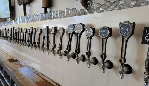 A row of beer taps with chalkboard labels for various flavors, set against a white wall.