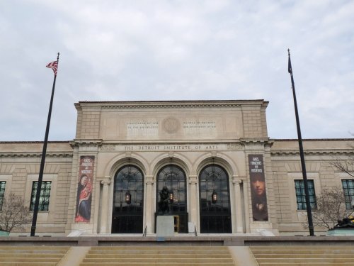 Facade of the Detroit Institute of Arts, featuring large windows and banners, with flags on either side.