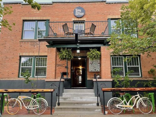 A brick building with a balcony, two bicycles outside, and greenery, featuring a sign that reads "Jam House."