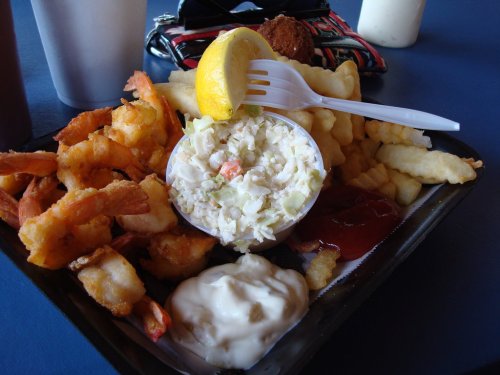 A plate of fried shrimp, coleslaw, fries, and dipping sauces, garnished with a lemon wedge.