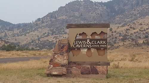 Sign for Lewis & Clark Caverns State Park, featuring a stone base and surrounded by mountainous terrain.