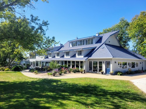 A large, modern house with a blue roof, surrounded by greenery and a well-maintained garden on a sunny day.