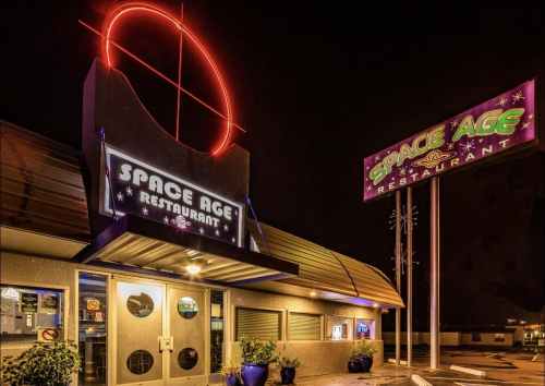 Exterior of Space Age Restaurant at night, featuring neon signs and a modern architectural design.