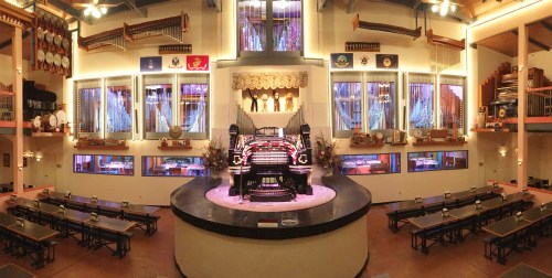 A grand organ in a spacious hall, surrounded by various musical instruments and colorful lights.