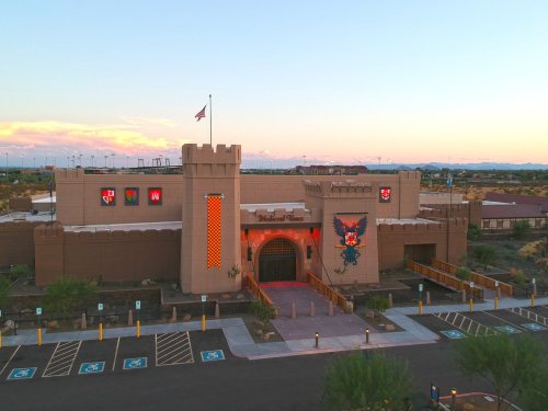 A large, castle-like building with a flag, colorful murals, and a parking lot under a sunset sky.