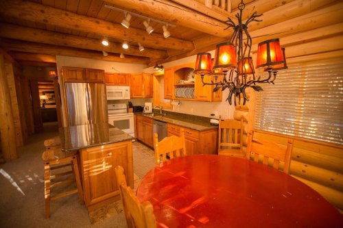 Cozy kitchen with wooden cabinets, granite countertops, and a round red dining table under a chandelier.