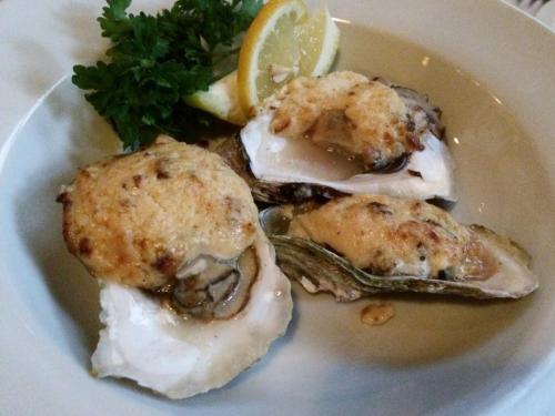 Baked oysters topped with a golden crust, garnished with lemon wedges and parsley on a white plate.