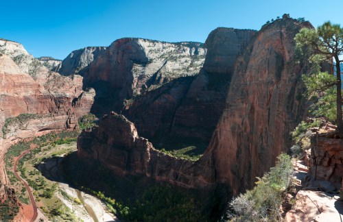 A panoramic view of Zion National Park, showcasing towering red rock formations and a winding river below.