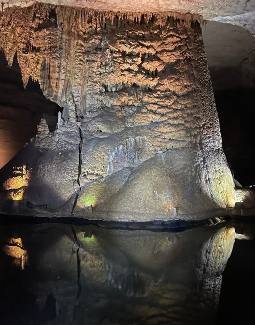 Stalactites and rock formations reflected in still water inside a dimly lit cave.