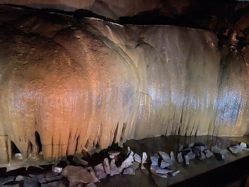 Stalactites and rock formations illuminated in a cave, reflecting warm colors on the wet surfaces.