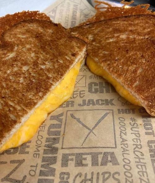 A close-up of a grilled cheese sandwich with melted cheese, resting on a patterned paper wrapper.