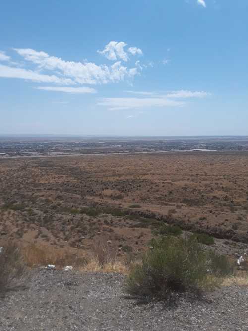 A wide view of a dry, arid landscape under a clear blue sky with scattered clouds.