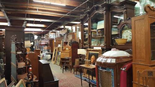 A spacious antique shop filled with various vintage furniture, decor, and collectibles arranged along the aisles.