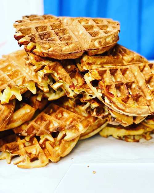 A stacked pile of golden-brown waffles on a white surface, with a blue background.