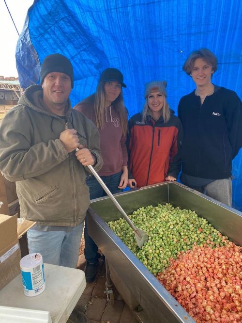 A group of four people stands by a large container filled with colorful popcorn, under a blue tarp.