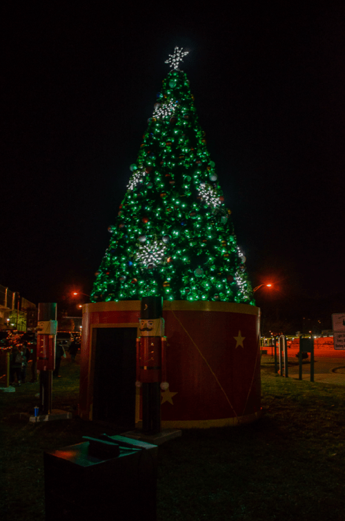 A large, illuminated Christmas tree with green lights and decorations, set against a night sky.