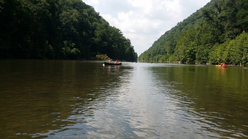 A serene river scene with lush green hills on either side and a small boat in the distance under a partly cloudy sky.
