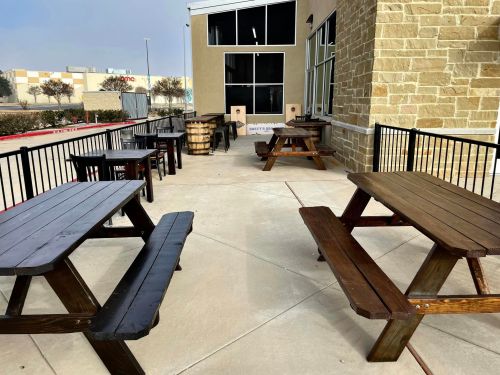 Outdoor seating area with wooden picnic tables and a barrel, next to a building.