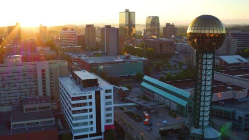 Aerial view of a city skyline at sunset, featuring a distinctive spherical tower and modern buildings.