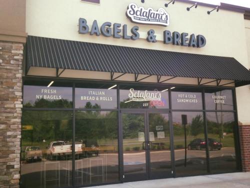 Exterior of a bagel and bread shop with a sign reading "Sclafani's Bagels & Bread," featuring large glass windows.