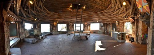 A spacious, rustic interior with wooden beams, stone flooring, and large windows, creating a cozy, natural atmosphere.
