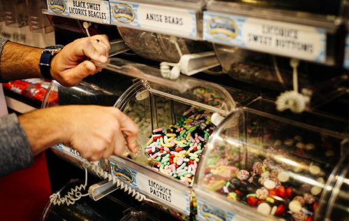A person scoops colorful candies from a display of assorted sweets in a candy store.