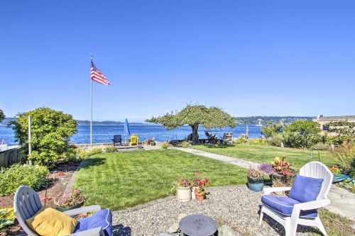 A scenic waterfront view featuring a lush lawn, garden, and seating area with an American flag waving in the breeze.