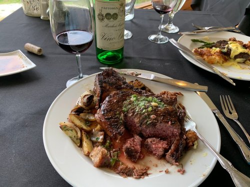 A plate of medium-rare steak with herbs, roasted potatoes, and a glass of red wine on a black tablecloth.