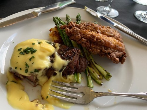 A plate featuring steak with hollandaise sauce, asparagus, and fried chicken, accompanied by cutlery.