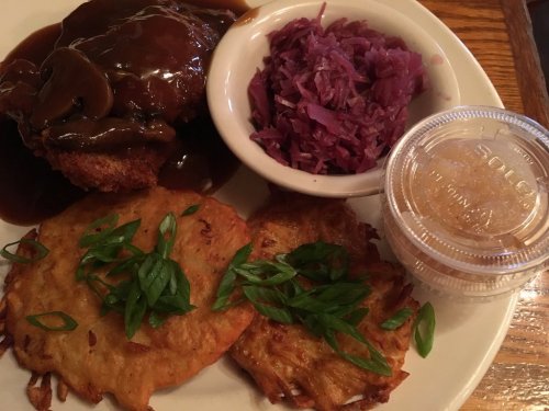 A plate featuring fried chicken with gravy, red cabbage, and two potato pancakes garnished with green onions.