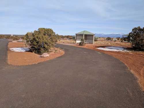 A winding road leads through a desert landscape with sparse vegetation and a small gazebo in the distance.