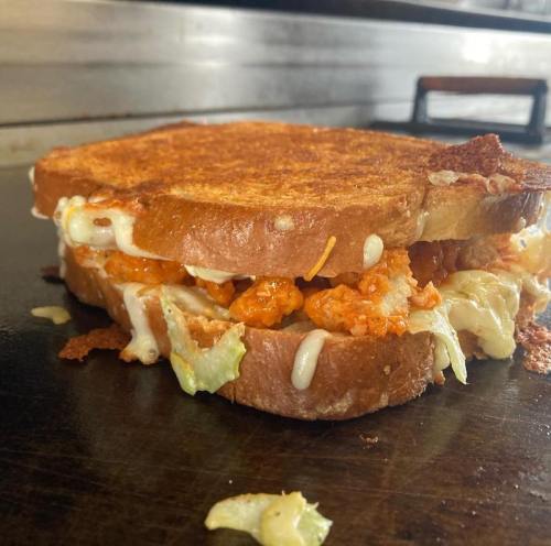 A close-up of a toasted sandwich filled with crispy chicken, lettuce, and melted cheese, resting on a grill.