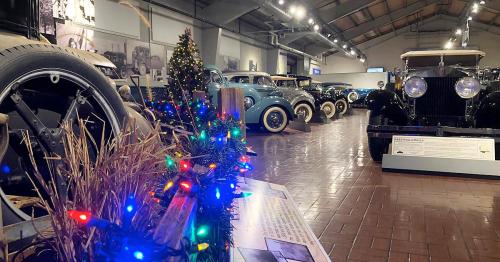 A vintage car museum display featuring classic cars and festive decorations with lights and greenery.