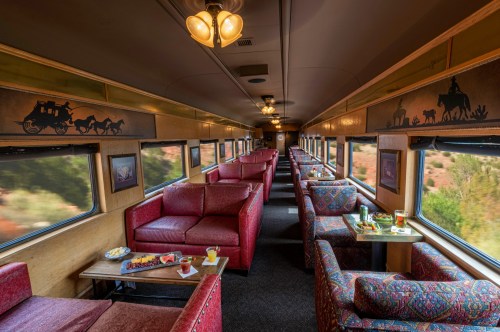 Interior of a vintage train car featuring red upholstered seating and tables, with scenic views through large windows.
