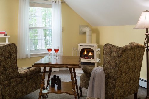 Cozy room with two armchairs, a small table with two glasses, and a fireplace, surrounded by soft yellow walls.