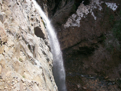A waterfall cascading down a rocky cliff, surrounded by sparse vegetation and remnants of snow.