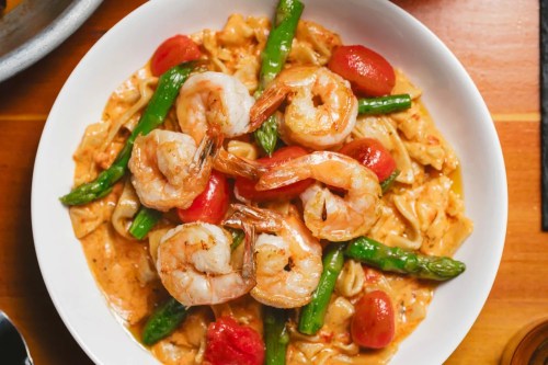 A bowl of pasta topped with shrimp, asparagus, and cherry tomatoes in a creamy sauce.