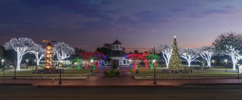 A festive park illuminated with colorful Christmas lights, featuring a decorated tree and glowing trees at dusk.