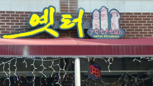 Sign for "yet/tuh" Korean Restaurant featuring colorful lettering and cartoonish figures on a brick wall.