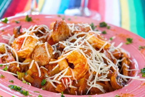 A colorful plate of shrimp and sausage pasta topped with shredded cheese, garnished with herbs on a vibrant tablecloth.