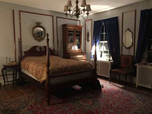 A cozy bedroom featuring a wooden bed, antique furniture, a chandelier, and dark blue curtains.