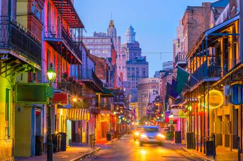 Vibrant street scene in New Orleans at dusk, featuring colorful buildings and city skyline in the background.